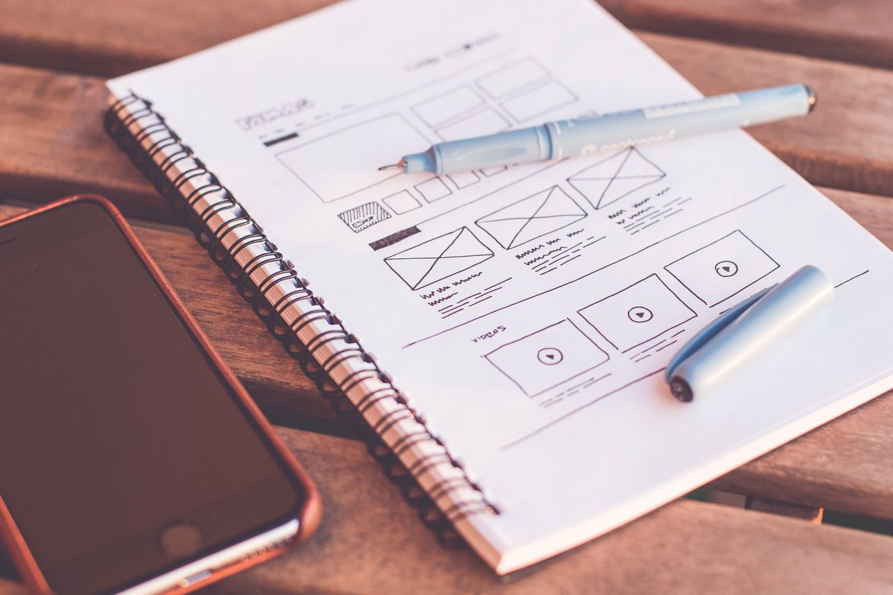 services-02 Gros plan sur un carnet avec des esquisses de wireframes et un smartphone posé sur un bureau en bois.